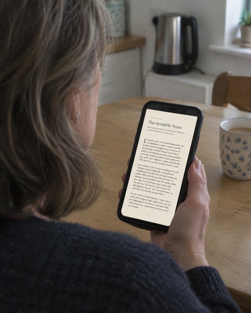 A woman seen from behind reading Chapter One on her phone at the kitchen table