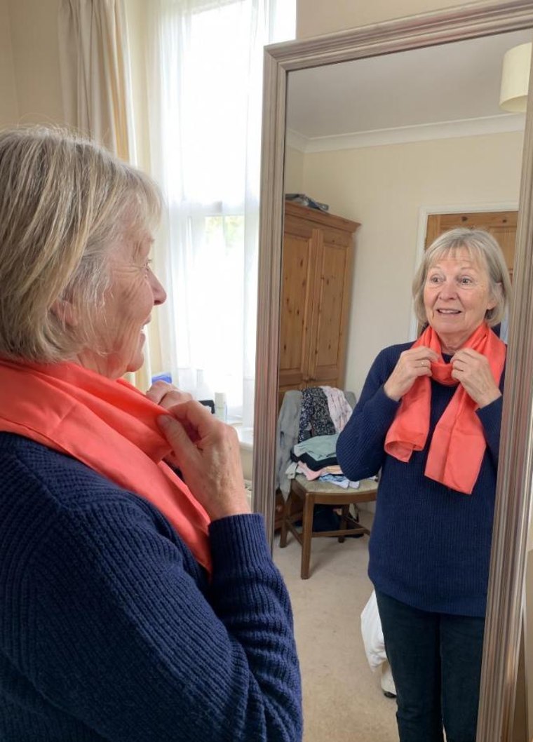 A woman in her late fifties trying on a coral scarf in front of a mirror